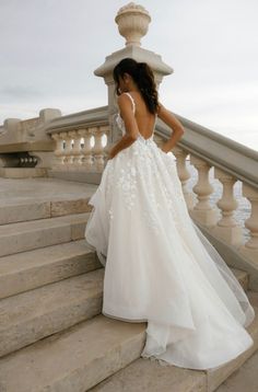 a woman in a wedding dress standing on some steps looking down at the ground with her back to the camera