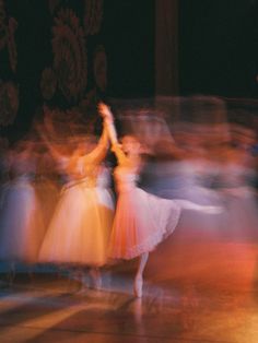 blurry photograph of dancers in motion on stage at an event or show, with people dressed in white and pink dresses