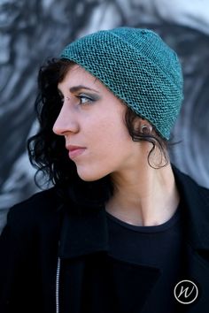 a woman wearing a green knitted beanie hat looking off to the side with her eyes closed