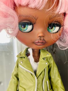 a close up of a doll with pink hair and blue eyes wearing a green leather jacket