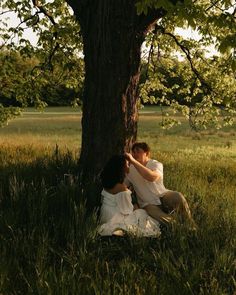 two people sitting under a tree in the grass