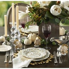 a table set for thanksgiving dinner with white and gold plates, silverware, wine glasses and flowers