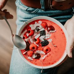 a person holding a bowl of smoothie topped with raspberries