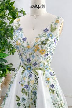 a white dress with blue and yellow flowers on the front, sitting on a mannequin