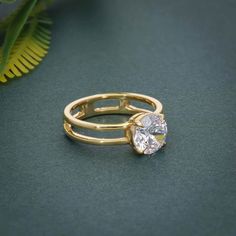 a gold ring with a heart shaped diamond in the center on a green surface next to a plant