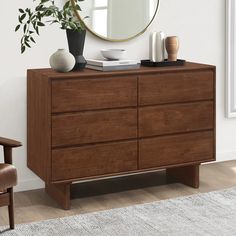 a wooden dresser with a mirror and vase on it in a white living room next to a chair