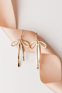 "🎀\"BOW\"🎀 them all away with the perfect set of dainty gold ribbons! Our Gold Ribbon Earrings feature a 14k gold filled hook and 14k gold filled ribbon.  Earrings measure approx. 1.8\" x .6\" Thank you so much for shopping with GGC! By supporting a small business, you are supporting a dream, a family, and so much more! We are so grateful for you! We hope to create with you again soon! ✨LOOKING FOR MORE EARRINGS?✨ Check out our other listings here: https://www.etsy.com/shop/GoldenGratitudeCol?ref=simple-shop-header-name&listing_id=1157209858§ion_id=37356619" Earrings Flatlay, Infinite Jewelry, Valentines Day Earrings, Jewelry Mood Board, Thanksgiving Jewelry, Ribbon Earrings, Photo Concept, Simple Hair, Polymer Clay Jewelry Diy