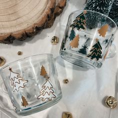 two glass cups sitting on top of a table next to each other with christmas trees painted on them