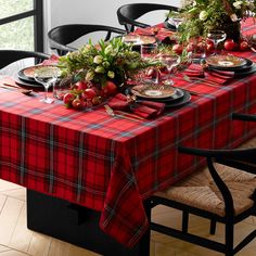 the table is set with red and black plaid cloths, plates, silverware, flowers and greenery