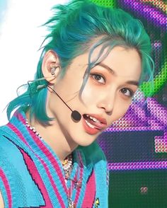 a woman with blue hair and piercings wearing a headset in front of a colorful background