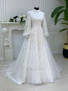 a white wedding dress on display in front of a table with flowers and greenery