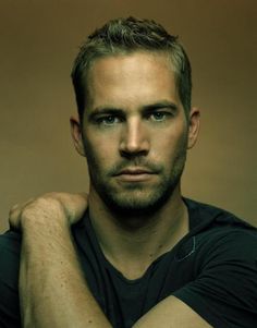 a man with his arms crossed looking at the camera while wearing a black t - shirt