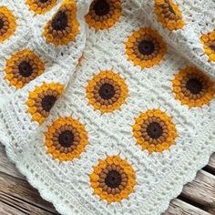 a crocheted blanket with sunflowers on it sitting on a wooden surface