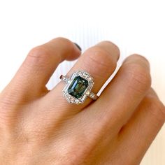 Blue Green Emerald Cut Sapphire Deco Halo Engagement Ring – Berlinger Jewelry Green Sapphire Ring With Baguette Cut, Gia Certified Square Cut Sapphire Diamond Ring, Emerald Cut Sapphire Ring With Baguette Diamonds, Sapphire Emerald Cut Rings With Baguette Diamonds, Fine Jewelry Sapphire Ring With Moissanite In Emerald Cut, Rectangular Emerald Ring With Diamond Accent Stones, Emerald Cut Moissanite Sapphire Ring In Fine Jewelry Style, Gia Certified Emerald Cut Green Sapphire Ring, Gia Certified Emerald-cut Green Sapphire Ring