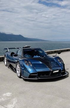 a blue and black sports car parked on the side of a road next to the ocean