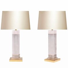 two clear glass lamps sitting next to each other on a wooden base with a beige shade