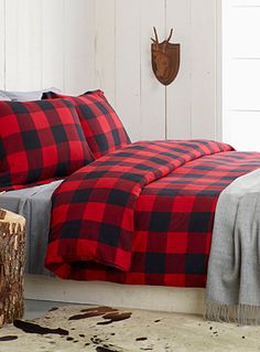 a red and black plaid comforter set on a white bed with wood stumps