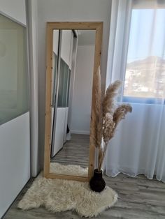 a large mirror sitting on top of a wooden floor next to a vase filled with dry grass