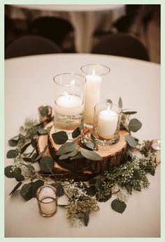 candles and greenery are arranged on top of a wooden slice at the center of a table