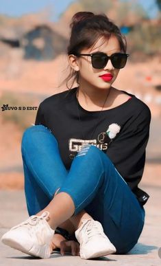 a woman sitting on the ground with her legs crossed wearing sunglasses and a black shirt