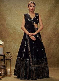 Embrace timeless elegance with the Black Mirror and Sequin Embroidered Lehenga set, a perfect blend of traditional allure and contemporary sophistication. Crafted from luxurious georgette, the flowing black lehenga is adorned with intricate gota and mirror work buttis, cascading gracefully into a striking sequin and zari embroidered border. Paired with a beautifully designed blouse, featuring mirror-embroidered buttis and accented with delicate pearl and mirror edges, this ensemble exudes opulence. The look is completed with a net dupatta, embellished with matching buttis and a coordinating border, adding an extra layer of grace. Designed for both style and convenience, this set includes a cancan for added volume and pockets for practicality, making it an ideal choice for Cocktail parties, Black Pre-draped Saree With Dupatta For Reception, Formal Black Pre-draped Saree With Resham Embroidery, Black Georgette Pre-draped Saree With Resham Embroidery, Evening Traditional Wear With Intricate Embroidery On Georgette, Evening Traditional Wear With Intricate Embroidery, Wedding Black Pre-draped Saree With Intricate Embroidery, Black Pre-draped Saree With Zari Work For Wedding, Elegant Black Saree For Navratri, Black Sharara For Evening Eid Festivities