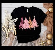 There's nothing more beautiful than a winter forest, and here's a unique version!!  This t-shirt features a grouping of pines, in pinks, and cheetah print! Festive stars add to this design!          A lovely tee for holiday parties, and any day throughout the season.  This t-shirt is everything you've dreamed of and more. It feels soft and lightweight, with the right amount of stretch. It's comfortable and flattering for all.  * 100% combed and ring-spun cotton (Heather colors contain polyester) Pink Graphic Print Christmas Tops, Pink Christmas Graphic Print Tops, Winter Pink Graphic Print T-shirt, Pink Graphic Print T-shirt For Winter, Pink Crew Neck T-shirt For Holidays, Pink Graphic Print T-shirt For Holiday, Pink Holiday Top With Graphic Print, Pink Graphic Print Top For Holiday, Pink Christmas T-shirt With Short Sleeves