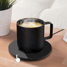 a black coffee mug sitting on top of a wooden table next to a potted plant