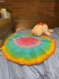 a crocheted rainbow blanket on top of a bed with a stuffed animal next to it