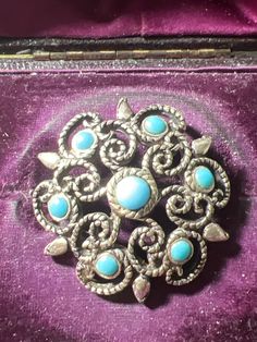 an old brooch with turquoise stones in it's case on purple velvet material