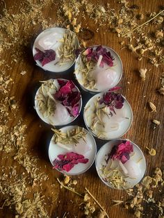 four white dishes with flowers on them sitting on a wooden table next to dried herbs