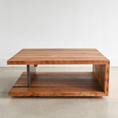 a wooden coffee table sitting on top of a cement floor next to a white wall