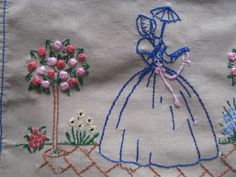 an embroidered piece of cloth with a woman holding an umbrella and flowers in the background