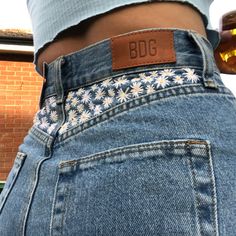 the back of a person's jeans with flowers on them and a beer in their pocket