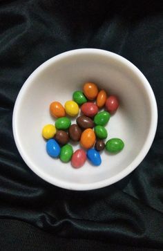 a white bowl filled with lots of colorful candies on top of a black cloth