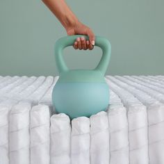 a person holding a teal colored kettle on top of a bed with white sheets