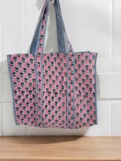 a pink and blue bag hanging from the side of a white tile wall next to a wooden shelf