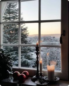 two candles are sitting on a window sill in front of the snow covered trees