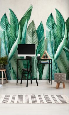 a living room with large green leaves on the wall and a desk in front of it