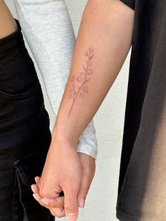 two people holding hands and one has a small flower tattoo on their left forearms