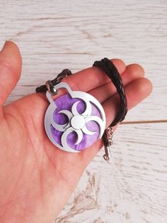 a hand holding a purple and white pendant on a brown string with a black cord