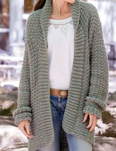 a woman standing in front of some rocks wearing a green cardigan sweater and jeans