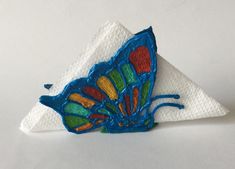 a blue butterfly sitting on top of a white paper napkin with red, yellow and green designs