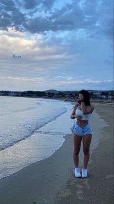 a woman standing on top of a sandy beach next to the ocean under a cloudy sky