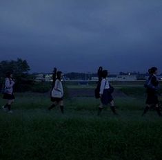 several people walking in the grass at night with backpacks on their backs and one person holding an umbrella