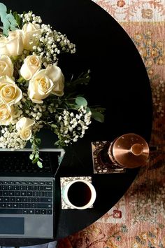 a laptop computer sitting on top of a table next to a bouquet of white roses