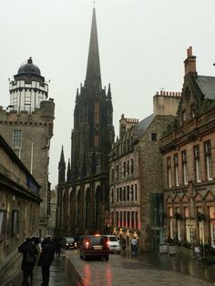 people are walking down the street in front of some old buildings with tall spires