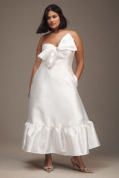 a woman wearing a white dress with a large bow on the front and bottom, standing in