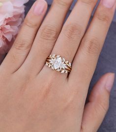 a woman's hand with two rings on it and flowers in the background next to her