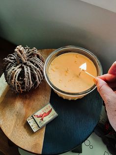 a person lighting a candle on top of a wooden table next to a small pumpkin