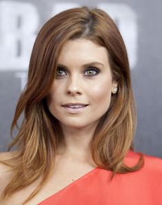 a woman with long brown hair and blue eyes wearing an orange one - shoulder dress